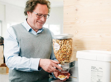 A man is standing at the nut dispenser, getting a serving of nuts.