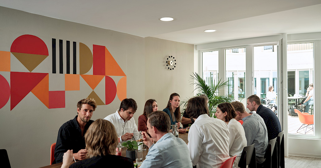 Coworkers having lunch together at a long table in the coworking kitchen at Grünhof Augustinerplatz