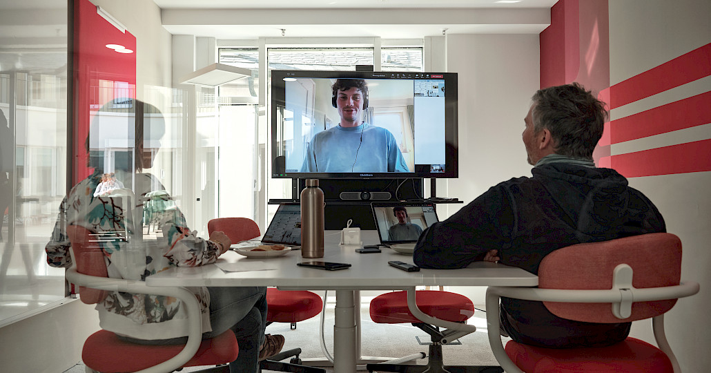 Two people hold video conference with large TV in meeting room 