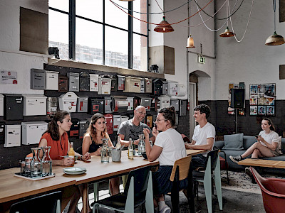 Coworker sitzen zusammen beim Community-Frühstücken zum Netzwerken, Synergien entwickeln und gemeinsam Kaffee trinken